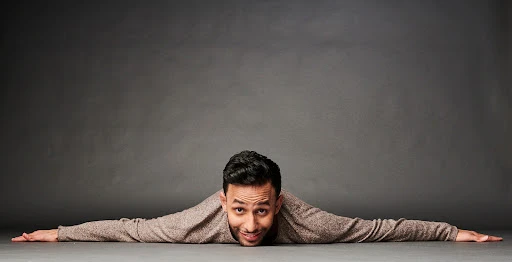 Adult male lying on the floor with his arms outstretched and smiling against a gray background in a photo studio setting.