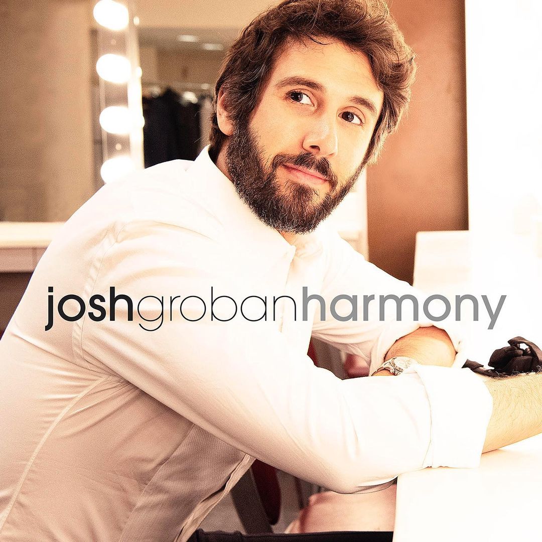 Josh Groban with a beard and white shirt leaning on a white surface in a dressing room, photographed by Andrew Eccles.
