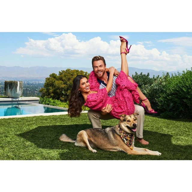 Man and woman pose playfully in a yard with a dog, featuring a pool and city views, under a bright sky, captured with natural light.