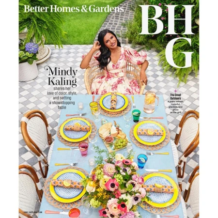 Magazine cover featuring Mindy Kaling sitting at an outdoor dining table with floral arrangements and place settings, captured eye-level.