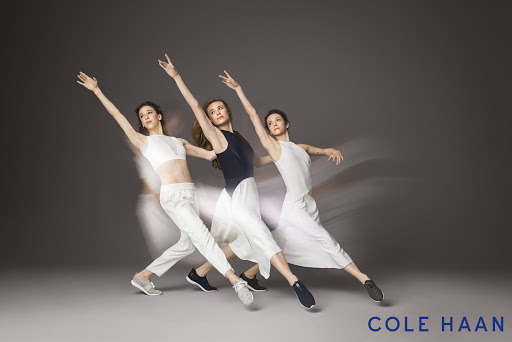 Three women in dance attire strike poses in a studio with motion blur, set against a gray backdrop, promoting dance and active lifestyle apparel.
