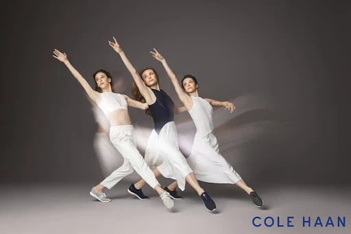Three women in dance attire strike poses in a studio with motion blur, set against a gray backdrop, promoting dance and active lifestyle apparel.