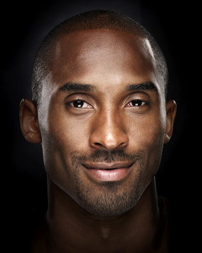 Portrait of a handsome adult male of African descent with a slight smile, set against a stark black background in a photo studio.