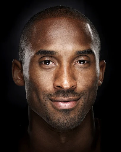 Portrait of a handsome adult male of African descent with a slight smile, set against a stark black background in a photo studio.