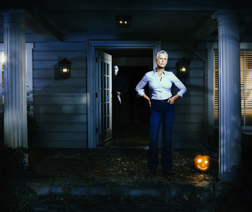 Jamie Lee Curtis stands in front of a suburban house, a Jack-o'-lantern to her right, while Michael Myers lurks in the doorway.