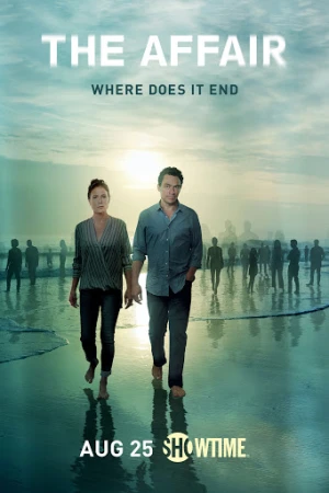 Man and woman walking barefoot on a wet beach at sunset with a crowd of silhouetted figures in the background.