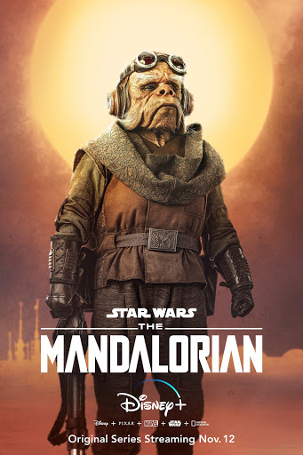 Character poster of the alien Ugnaught Kuiil from Star Wars: The Mandalorian, in earth-tone garments and headgear, against an orange sky.