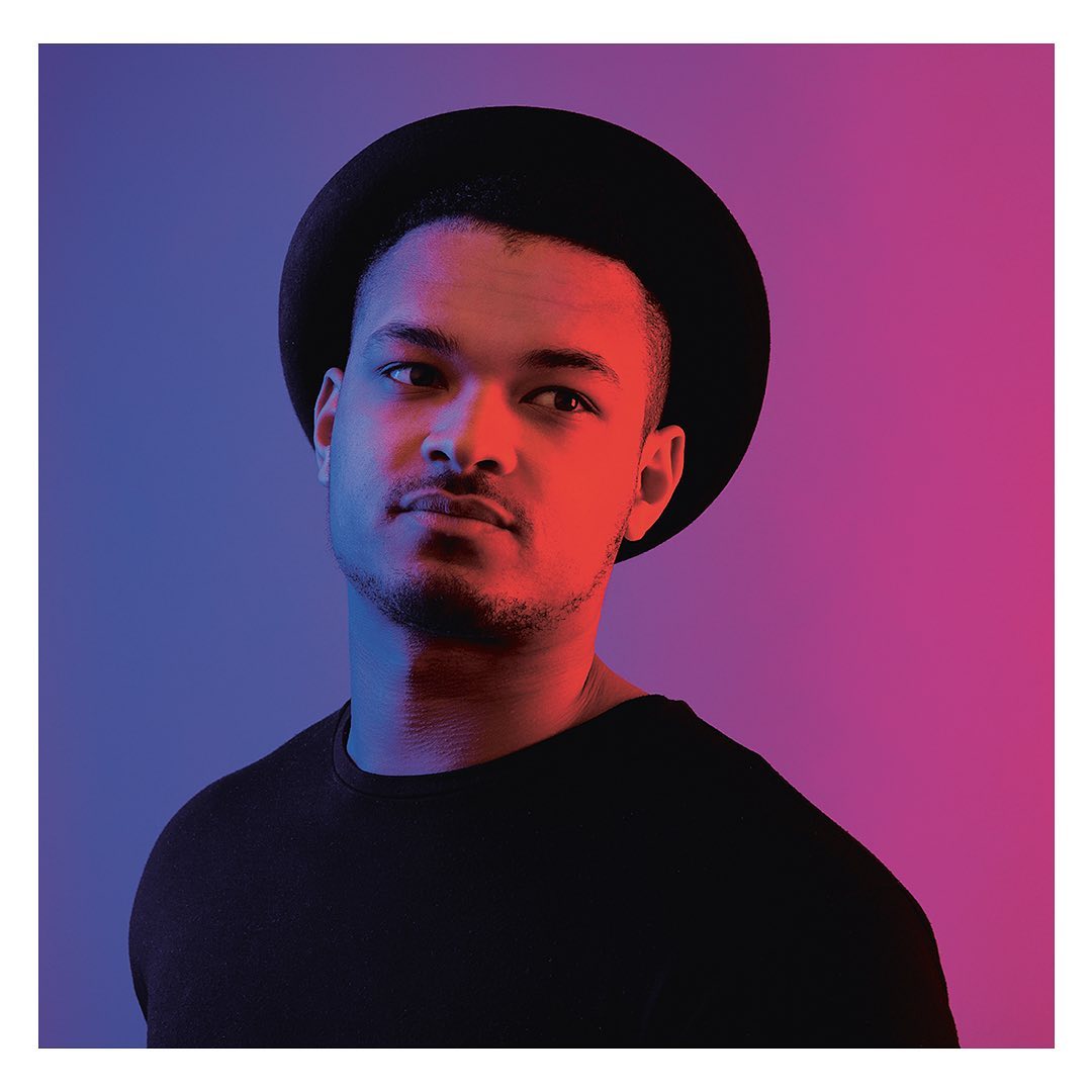 Portrait of a person in a hat, looking to the left, with red and blue lighting effects on their face and in the background.