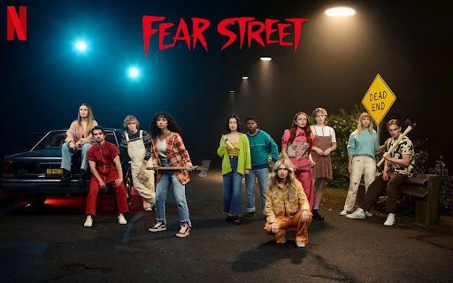 Group of young adult actors stand together on a street at night with an old car, an axe, and a Dead End sign in a horror movie scene.