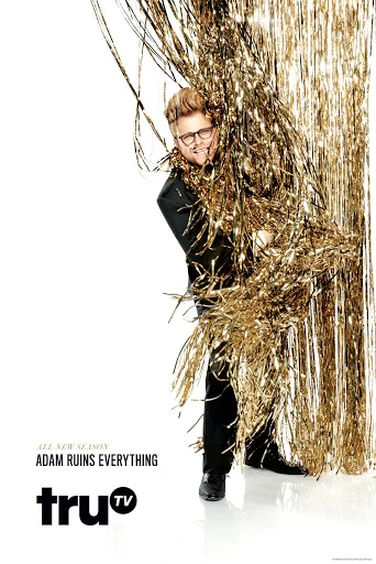 Promotional shot for the television show Adam Ruins Everything, featuring Adam Conover partially visible behind gold streamer curtains.