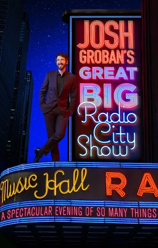 Josh Groban stands next to a neon sign for his 'Great Big Radio City Show' in front of a high-rise building at night with stars.