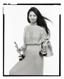 Portrait of Chloé Zhao holding two Oscar statuettes against a plain white background by photographer Andrew Eccles.