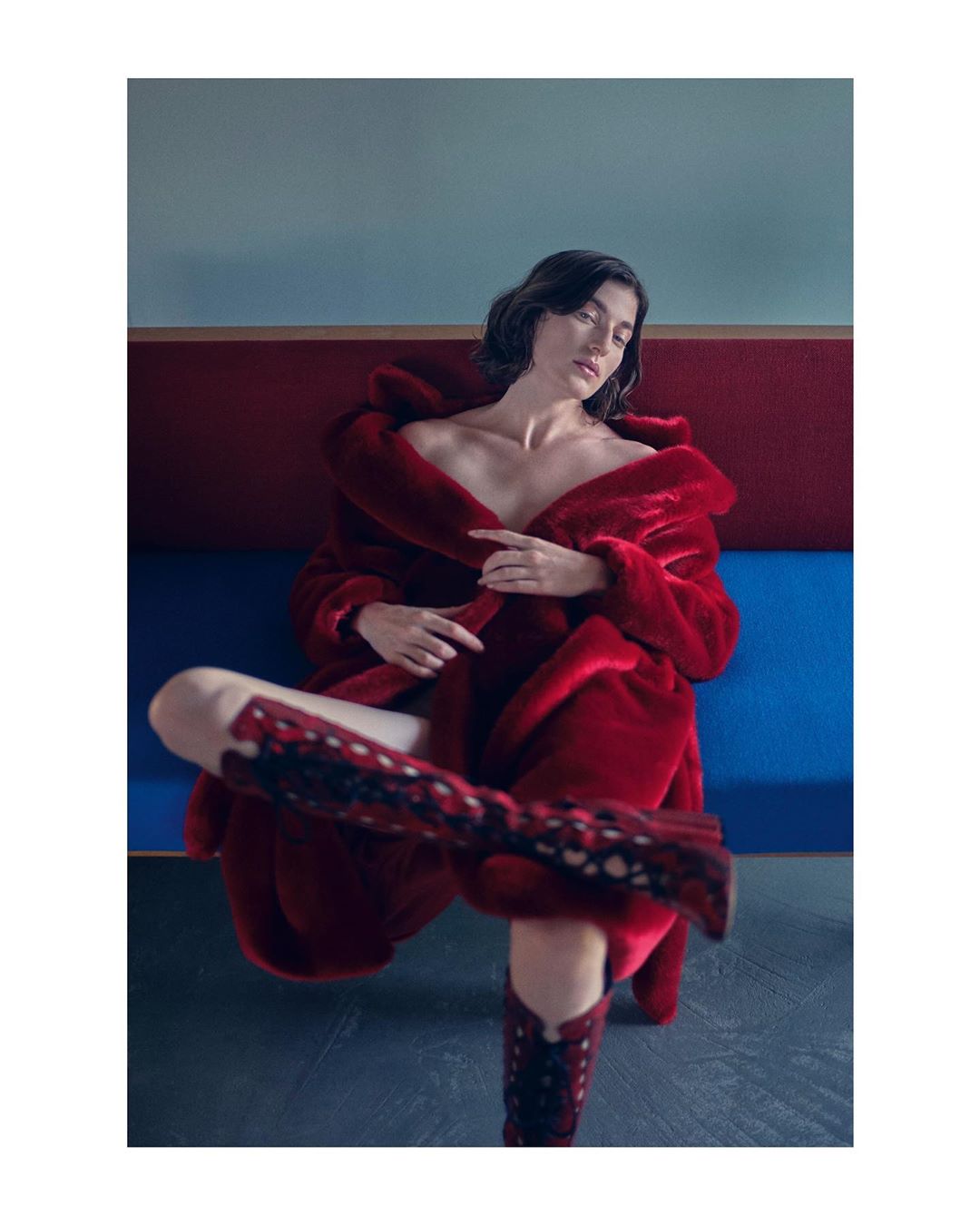 Brunette model in red faux fur coat and matching patterned boots sits against a geometric backdrop of blue, red and brown.