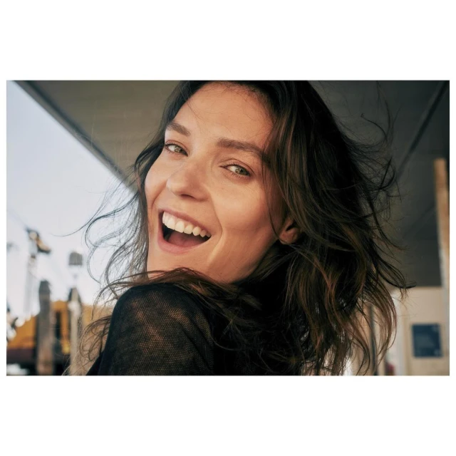Close-up portrait of a smiling adult woman with brown hair looking at the camera. She has white teeth and a joyful expression.