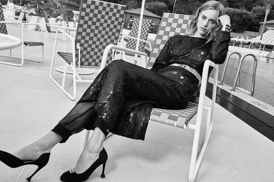 Woman in sequined outfit seated on poolside lounge chair photographed by Arnaud Pyvka in monochrome.