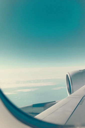 Airplane wing and engine viewed from the window seat with a clear, teal sky in the background, conveying air travel and flight.