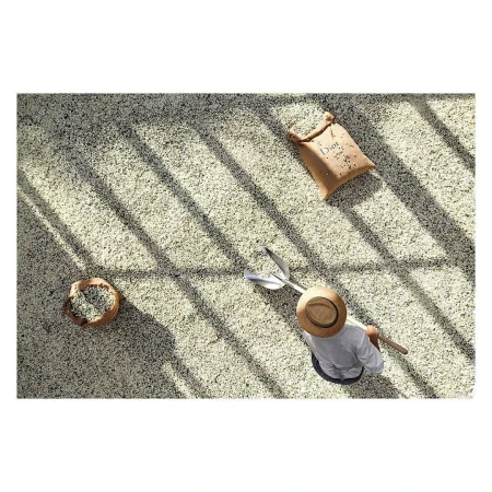 Overhead shot of an adult wearing a straw hat and working on a coffee bean farm with a metal shovel under the bright sun.