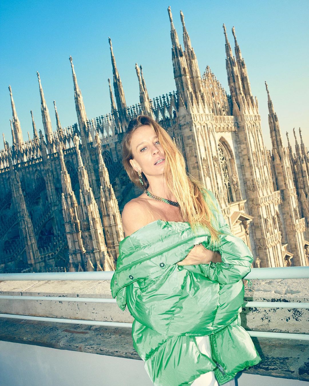 Woman in an off-shoulder jacket standing in front of the Milan Cathedral, Italy, with a bright blue sky in the background.