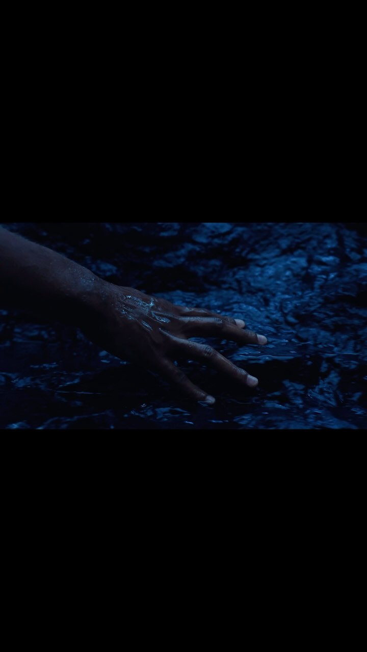 Human hand submerged in blue water with subtle ripples and contrasting light and shadows, creating a visually striking composition.