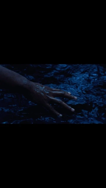 Human hand submerged in blue water with subtle ripples and contrasting light and shadows, creating a visually striking composition.