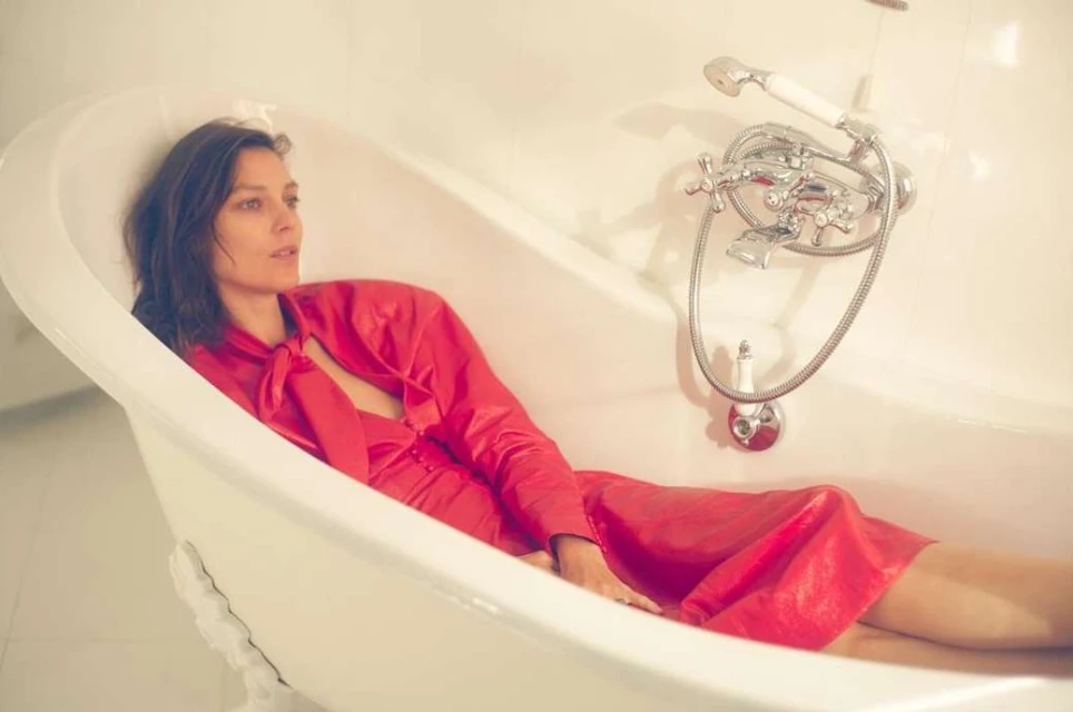 A woman in a red dress reclines in a white clawfoot bathtub, her relaxed pose complemented by the neutral bathroom setting.