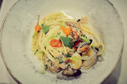 Overhead shot of a plate of spaghetti alle vongole with clams, parsley, and peppers in a light sauce, served in a shallow dish.