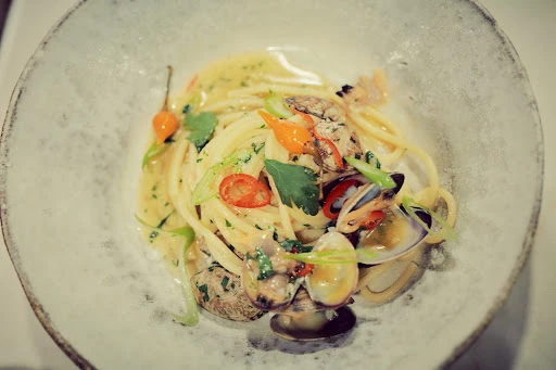 Overhead shot of a plate of spaghetti alle vongole with clams, parsley, and peppers in a light sauce, served in a shallow dish.