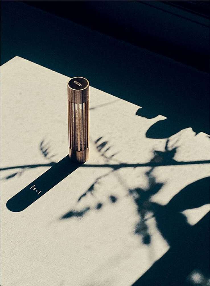 Close-up of a modern bronze-colored cylindrical table lamp casting shadows on a light surface, creating contrast and a minimalist aesthetic.