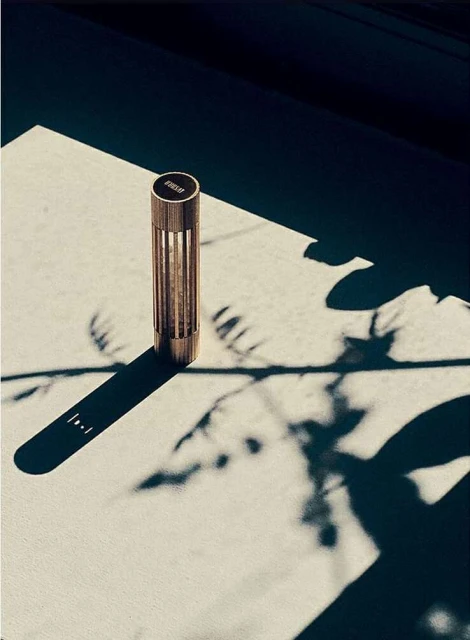 Close-up of a modern bronze-colored cylindrical table lamp casting shadows on a light surface, creating contrast and a minimalist aesthetic.