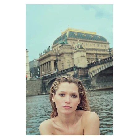 Portrait of a woman with wet hair standing before a river with a grand European bridge and historical building in the background