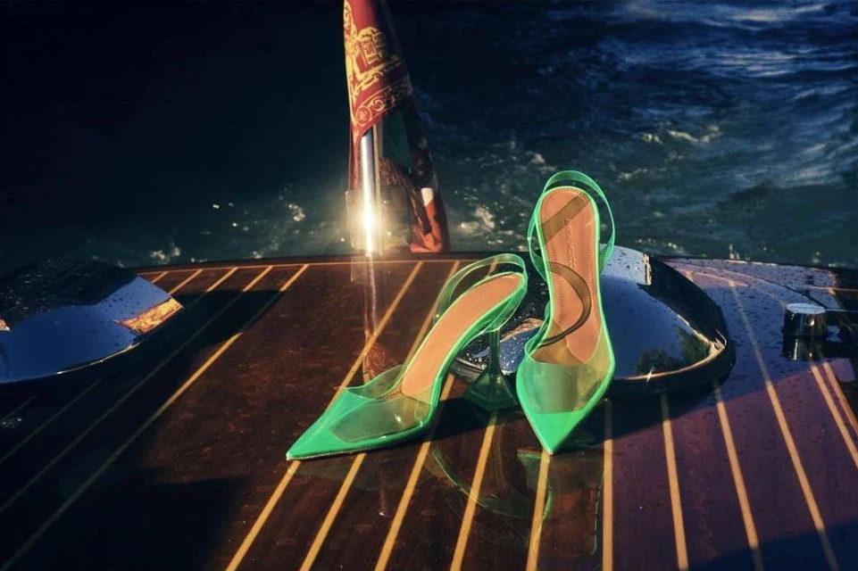 Elegant green slingback high heels on a boat deck with a red and gold flag in the background, creating a sophisticated fashion image.