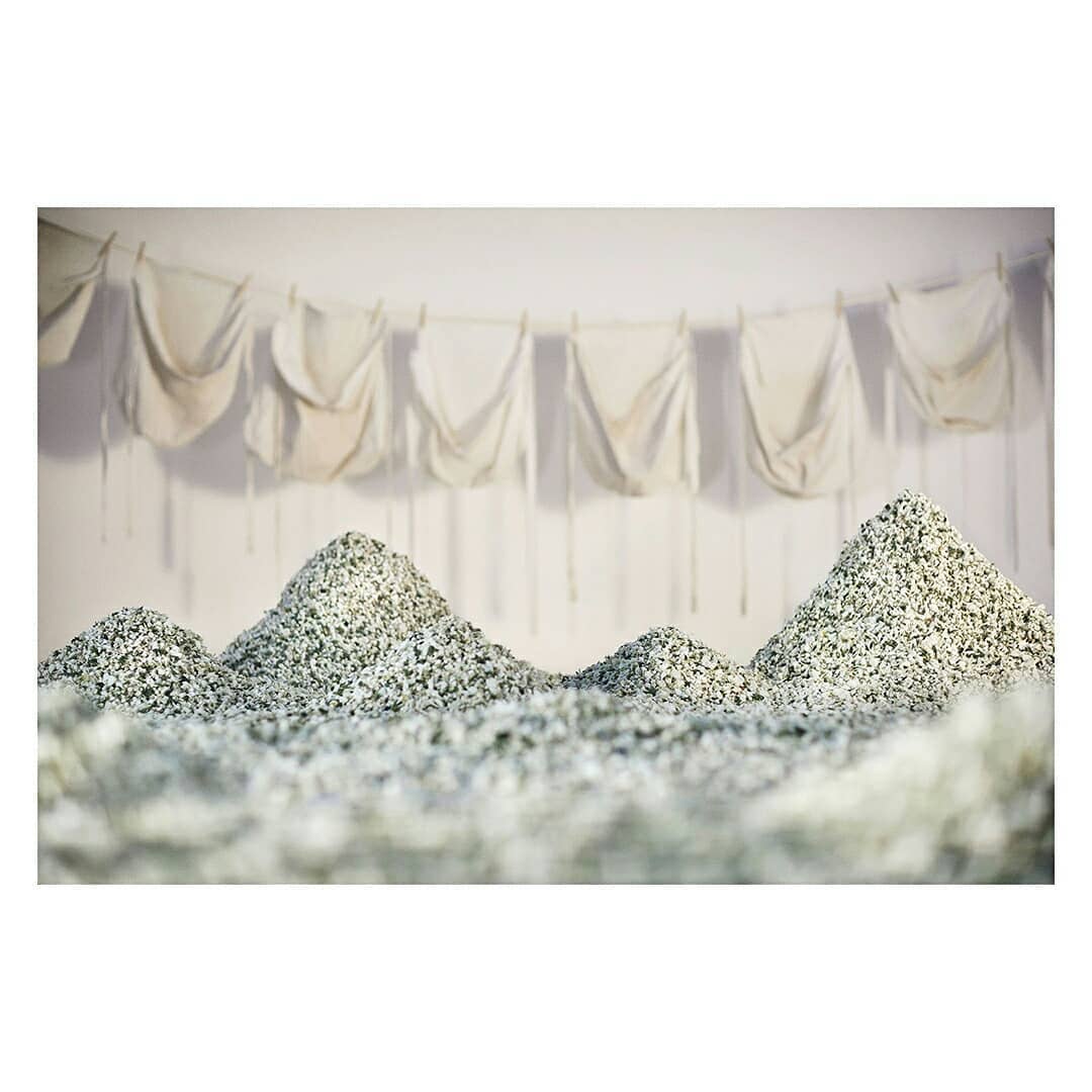 Abstract art: Piles of textured materials resembling mountains in an indoor setting, with white fabrics hanging in the background.