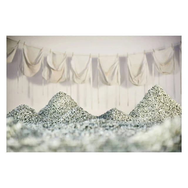 Abstract art: Piles of textured materials resembling mountains in an indoor setting, with white fabrics hanging in the background.