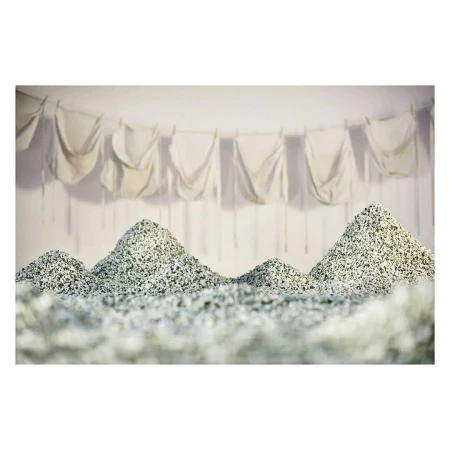 Abstract art: Piles of textured materials resembling mountains in an indoor setting, with white fabrics hanging in the background.