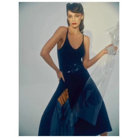 Woman in a dark blue slip dress with a pleated panel holding translucent plastic against a plain white background.