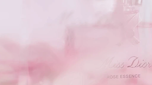 Close-up of Miss Dior Rose Essence perfume bottle with silver text on a soft pink background, product shot for beauty and fashion.