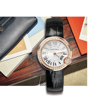 Elegant wrist watch on a table with books and a dark-blue leather wallet, presented in a well-lit, high-angle product shot.