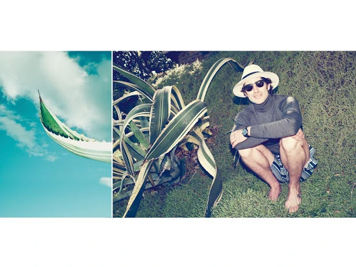 Adult male squats on green grass near succulent plants, wearing a hat and sunglasses in a sunny, daytime outdoor setting.