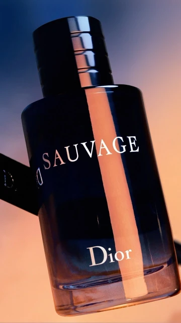 Close-up studio shot of a dark-blue Dior Sauvage perfume bottle against a blurred gradient background. The bottle features silver lettering.