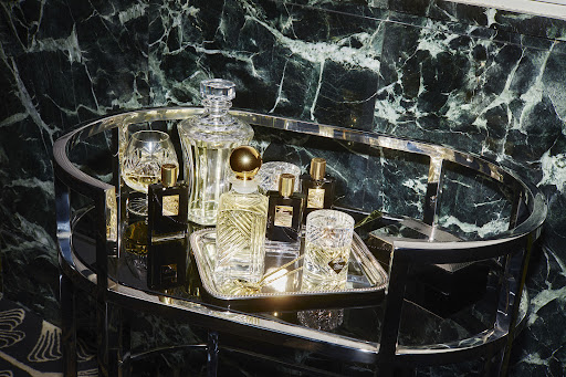 Crystal decanter and perfume bottles on a mirrored chrome bar cart against a dark marble wall, in a beauty or interior setting.