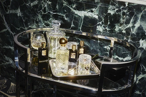 Crystal decanter and perfume bottles on a mirrored chrome bar cart against a dark marble wall, in a beauty or interior setting.