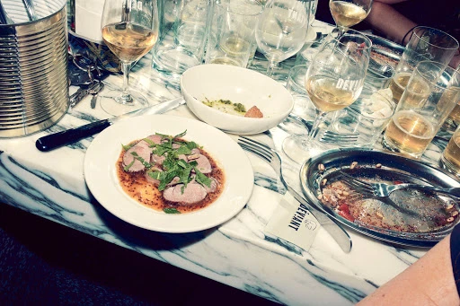 Overhead shot of a table covered with a plate of sliced meat and herbs, wine glasses, an empty bowl, cutlery, and used dishes.