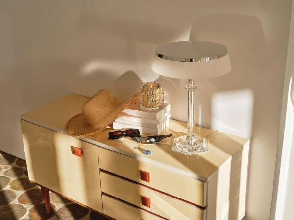 Crystal table lamp and straw hat on a wooden sideboard in warm natural light