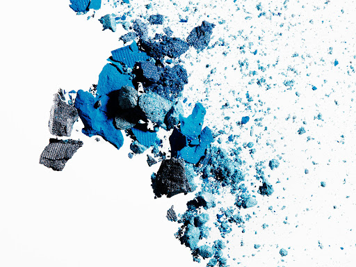 Close-up of crushed eye shadow pigment in shades of blue and grey, scattered on a white surface, beauty and cosmetic concept.