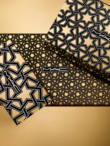 Geometric pattern of tessellated black stars on gold cosmetic product packaging featuring the MAC logo in the center of the image.