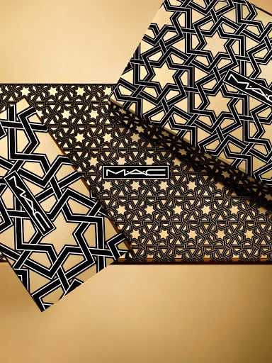Geometric pattern of tessellated black stars on gold cosmetic product packaging featuring the MAC logo in the center of the image.