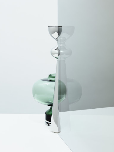 Still life photography featuring a tall metallic candlestick and a green glass vase seen through a tinted glass panel.