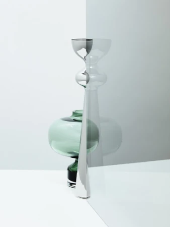 Still life photography featuring a tall metallic candlestick and a green glass vase seen through a tinted glass panel.