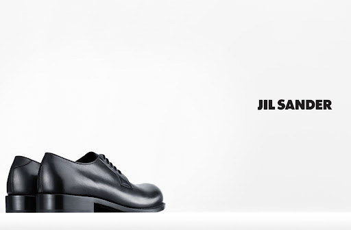 Studio product shot of pair of black leather lace-up dress shoes on white background with Jil Sander logo text.