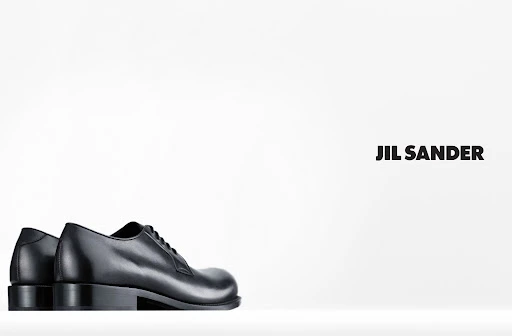 Studio product shot of pair of black leather lace-up dress shoes on white background with Jil Sander logo text.